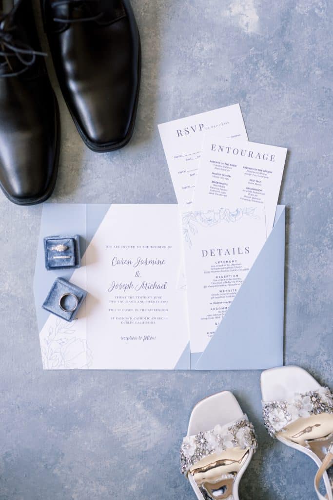 White and blue wedding invitation styled with a blue ring box and engagement ring, bride and groom shoes