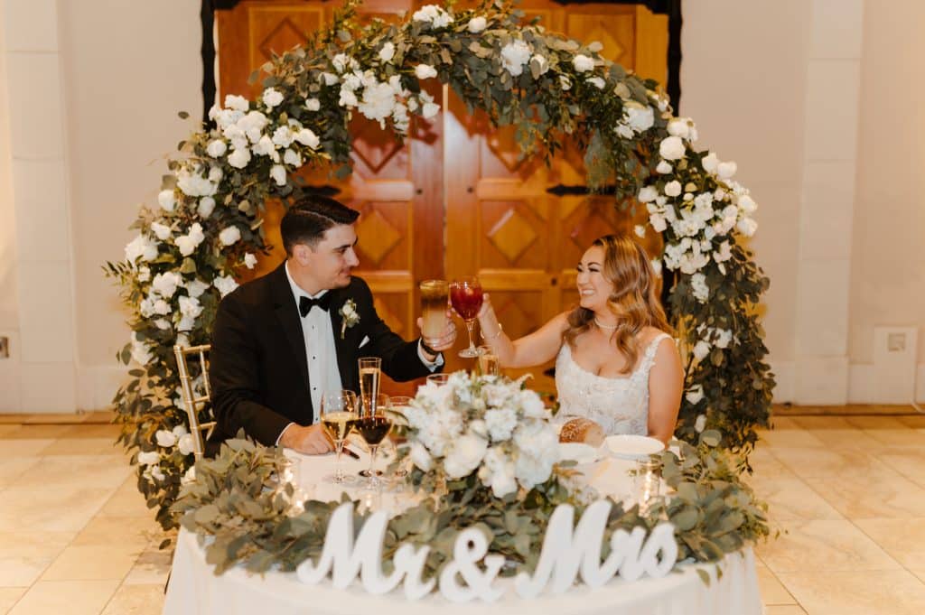 Stirling and Tyler sitting at a sweetheart table under a floral arch