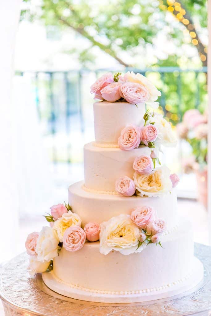 White wedding cake with four tiers with pink and cream garden roses 